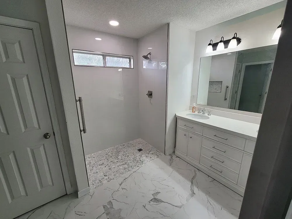 A bathroom with a walk in shower , sink and mirror.
