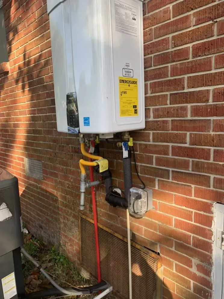 A gas water heater is attached to a brick wall.
