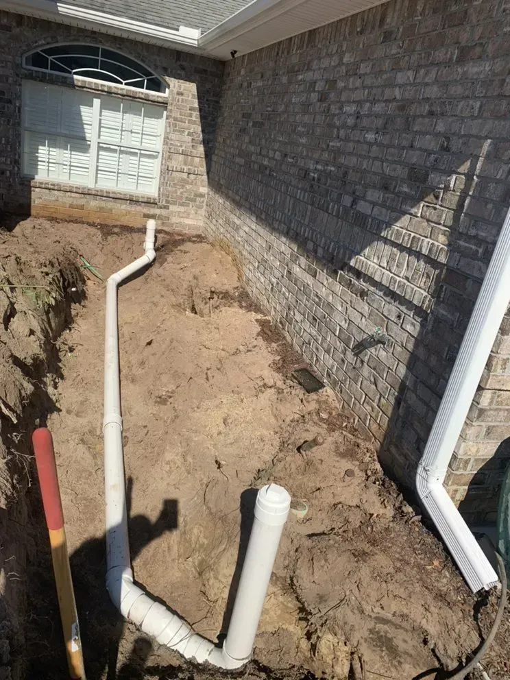 A drain pipe is being installed on the side of a brick house.