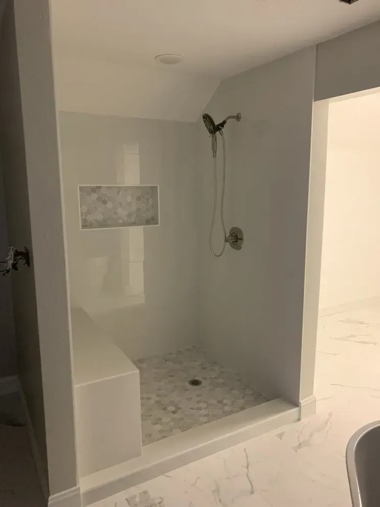A bathroom with a walk in shower with a bench and a shower head.