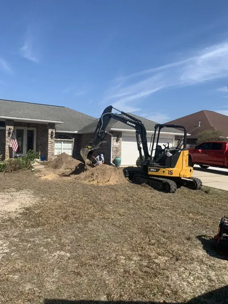 A yellow excavator is digging a hole in the dirt in front of a house.