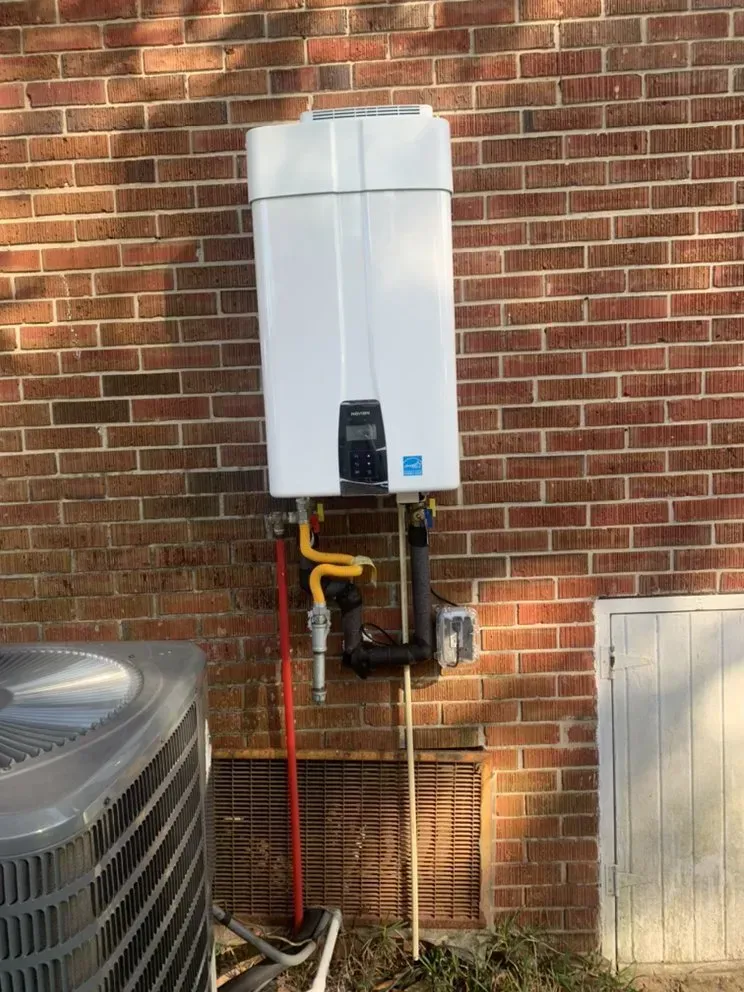 A white water heater is mounted on a brick wall next to an air conditioner.