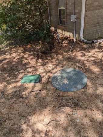 A septic tank is sitting in the dirt in front of a house.