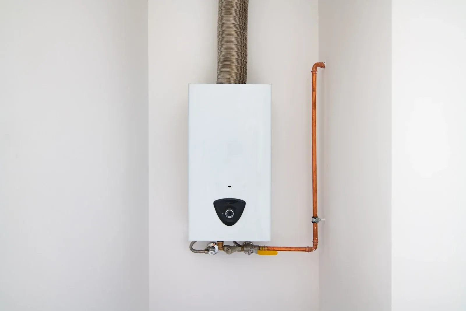 A white water heater is hanging on a white wall next to a copper pipe.