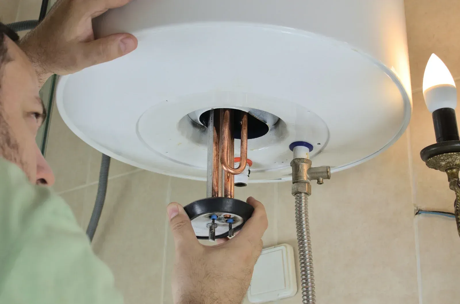 A man is fixing a water heater in a bathroom.