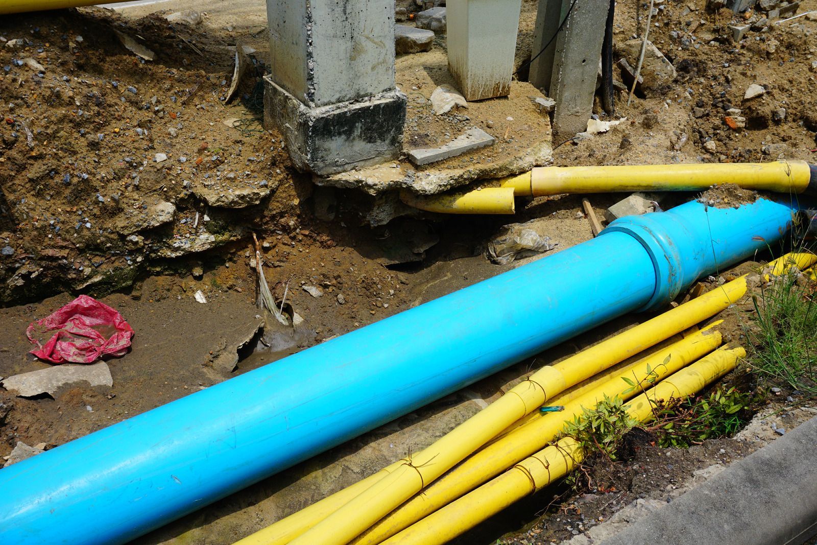 A blue pipe and yellow pipes are laying in the dirt.
