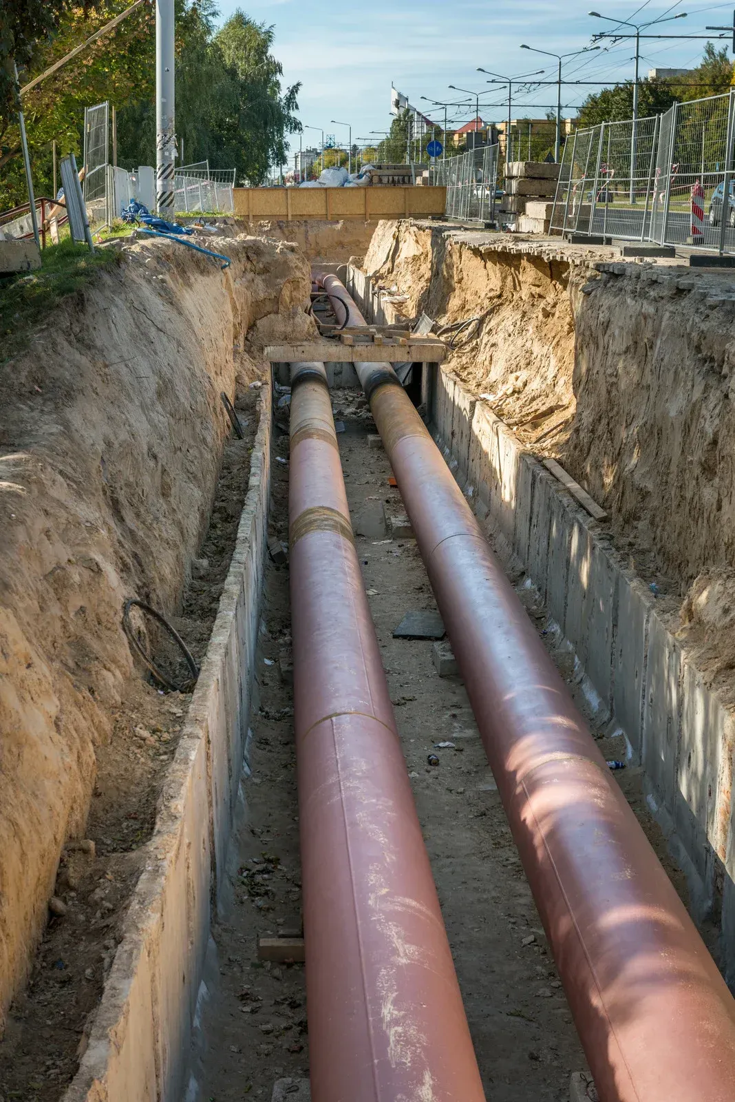 Two red pipes are being installed in a trench.