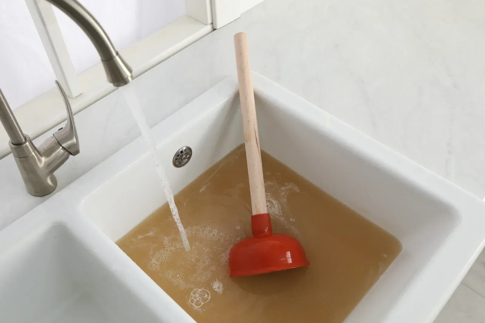 A sink with brown water and a red plunger in it.