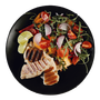 Grilled chicken and salad with tomatoes, red onion, and lime on a black plate.