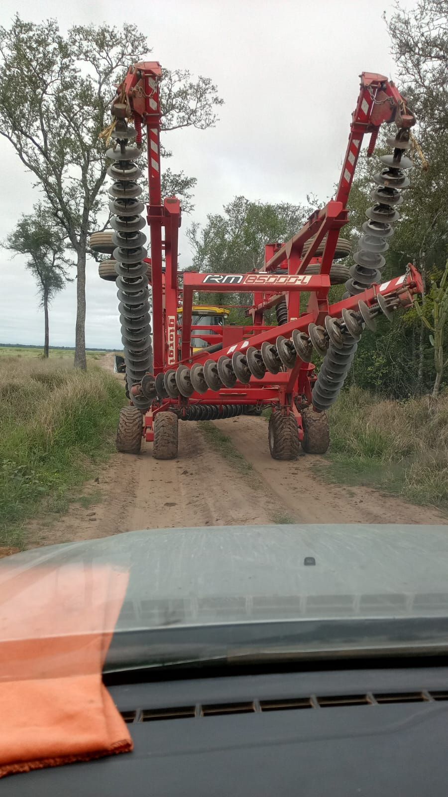 Una gran grada de discos agrícola roja está plegada en posición de transporte en un camino de tierra