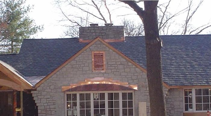 Stone house roof with a central dormer, orange trim, and leafless trees in front