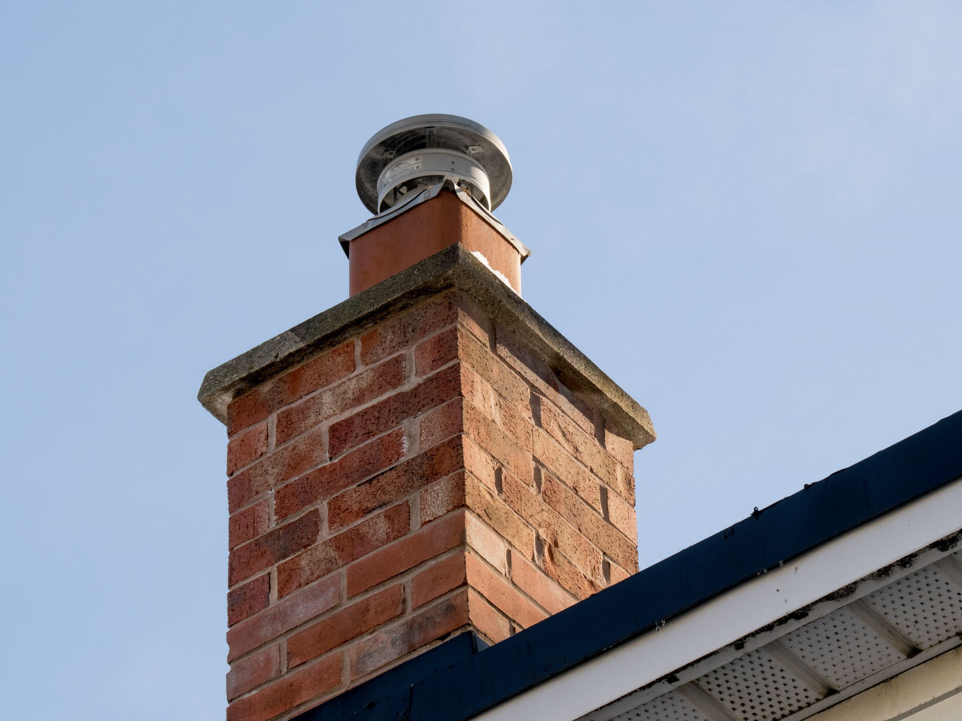 A brick chimney on top of a house with a blue roof.
