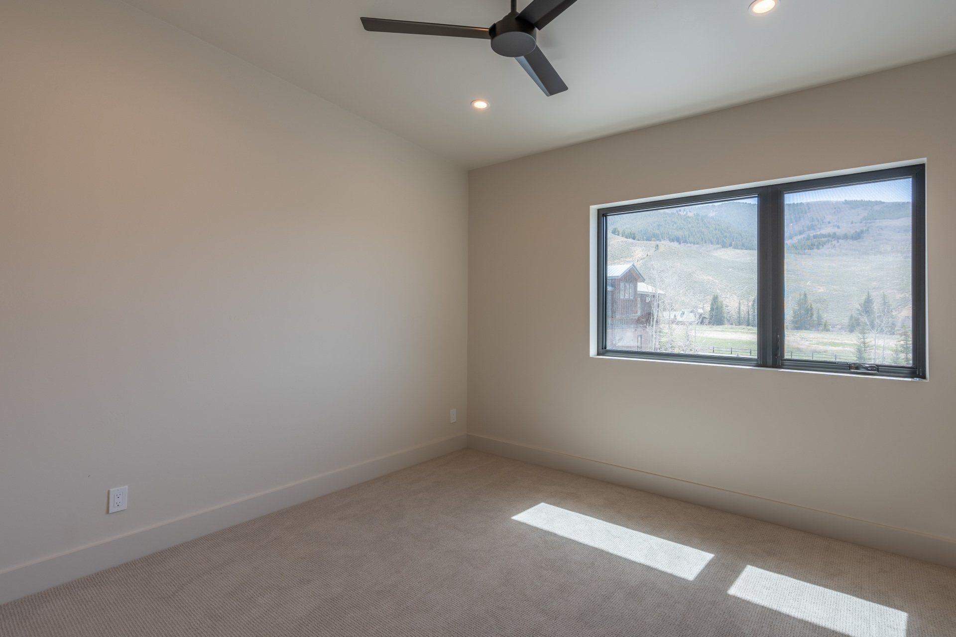 An empty bedroom with two windows and a ceiling fan.