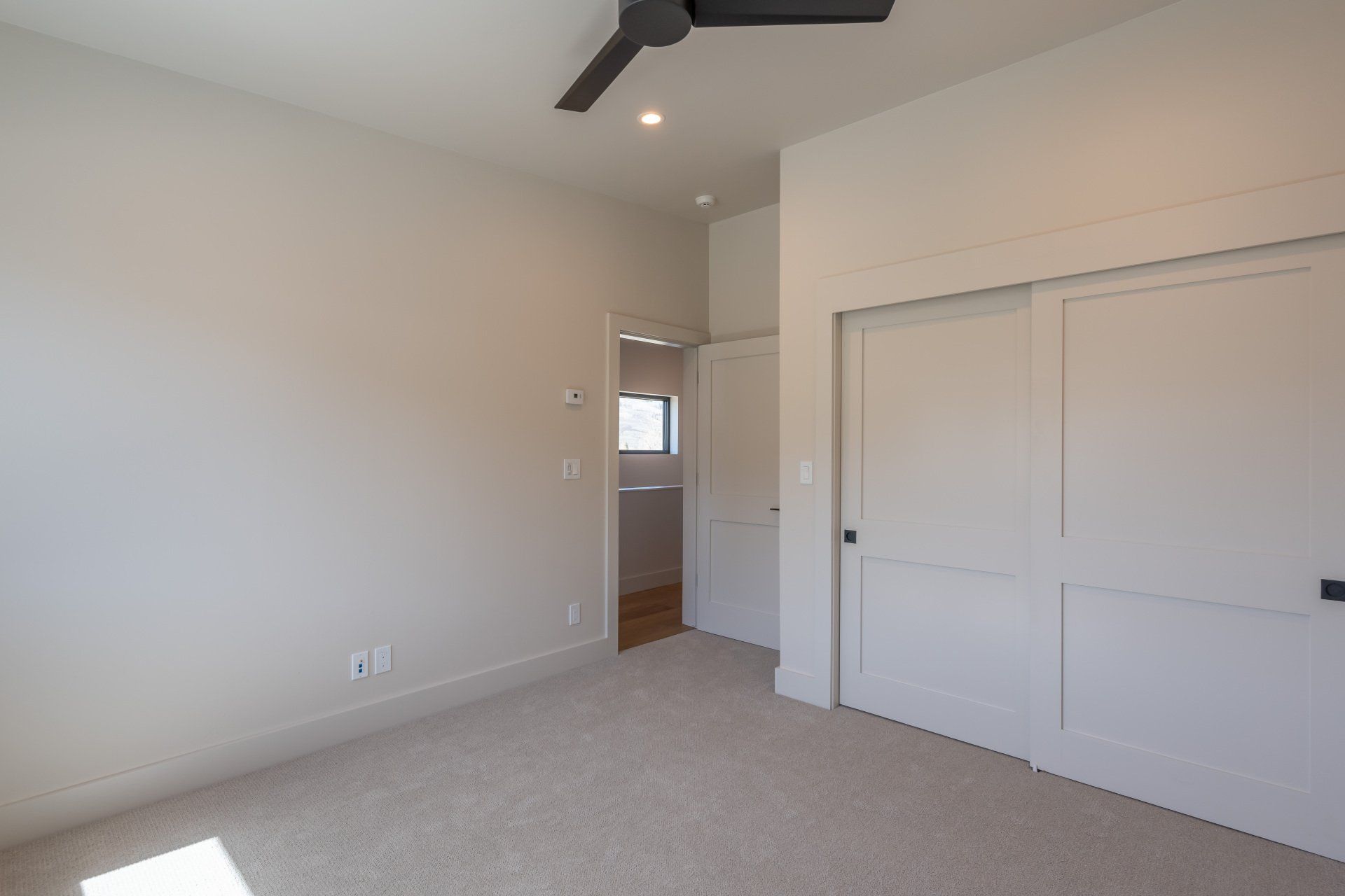 An empty bedroom with a ceiling fan and sliding doors.