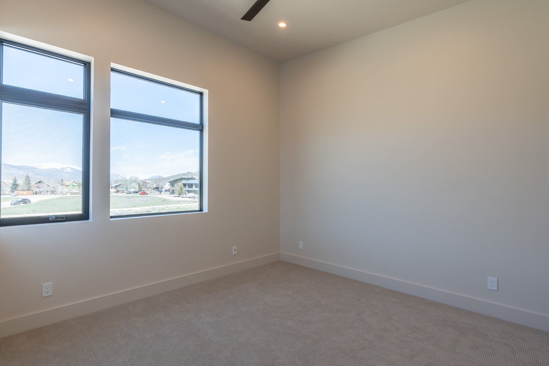 An empty bedroom with two windows and a ceiling fan.