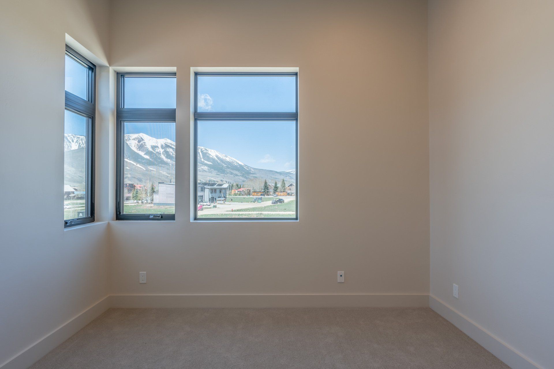 An empty room with two windows and a view of a mountain.
