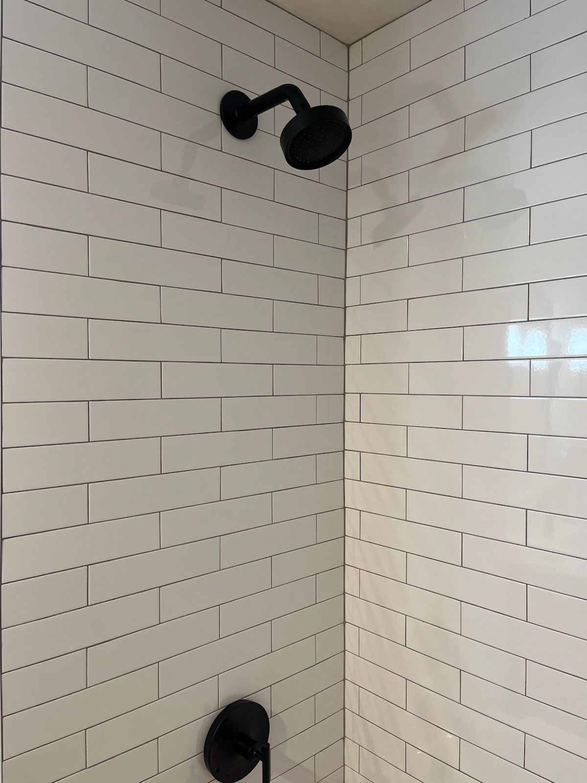A shower with white tiles and a black shower head