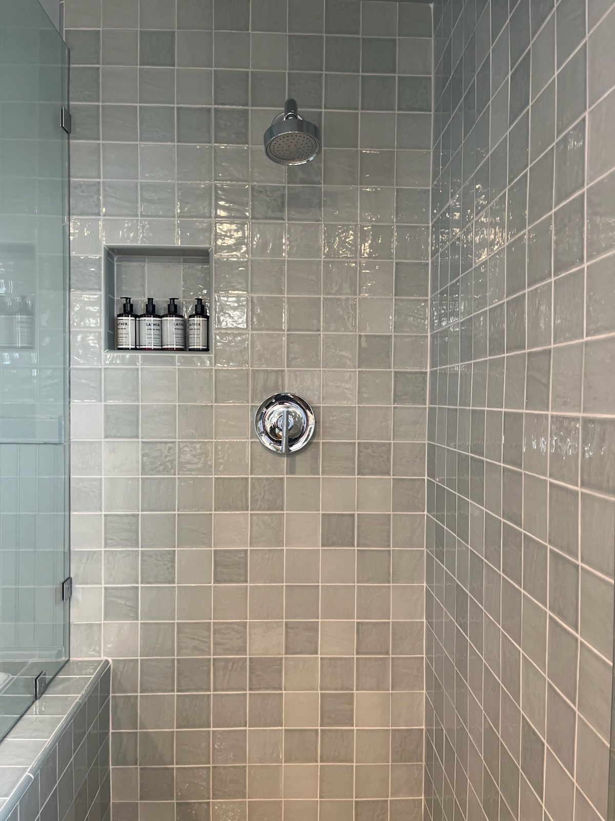 A shower with white tiles and a glass door.