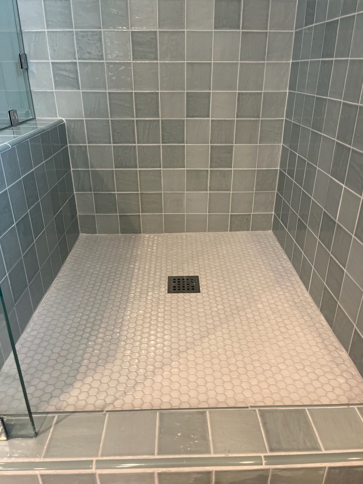 A walk in shower with gray tiles and a drain.