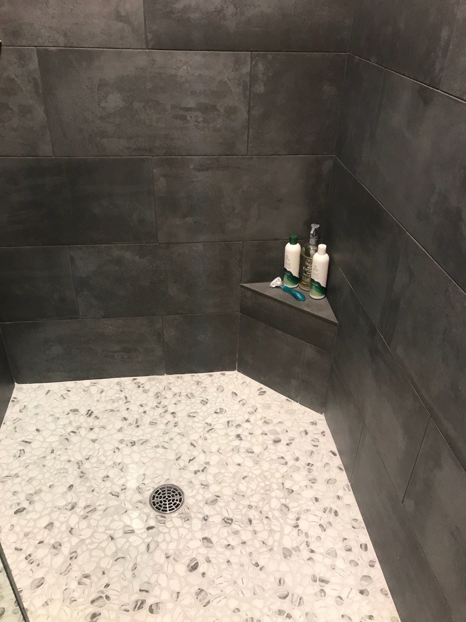 A shower stall with a corner shelf and a drain.