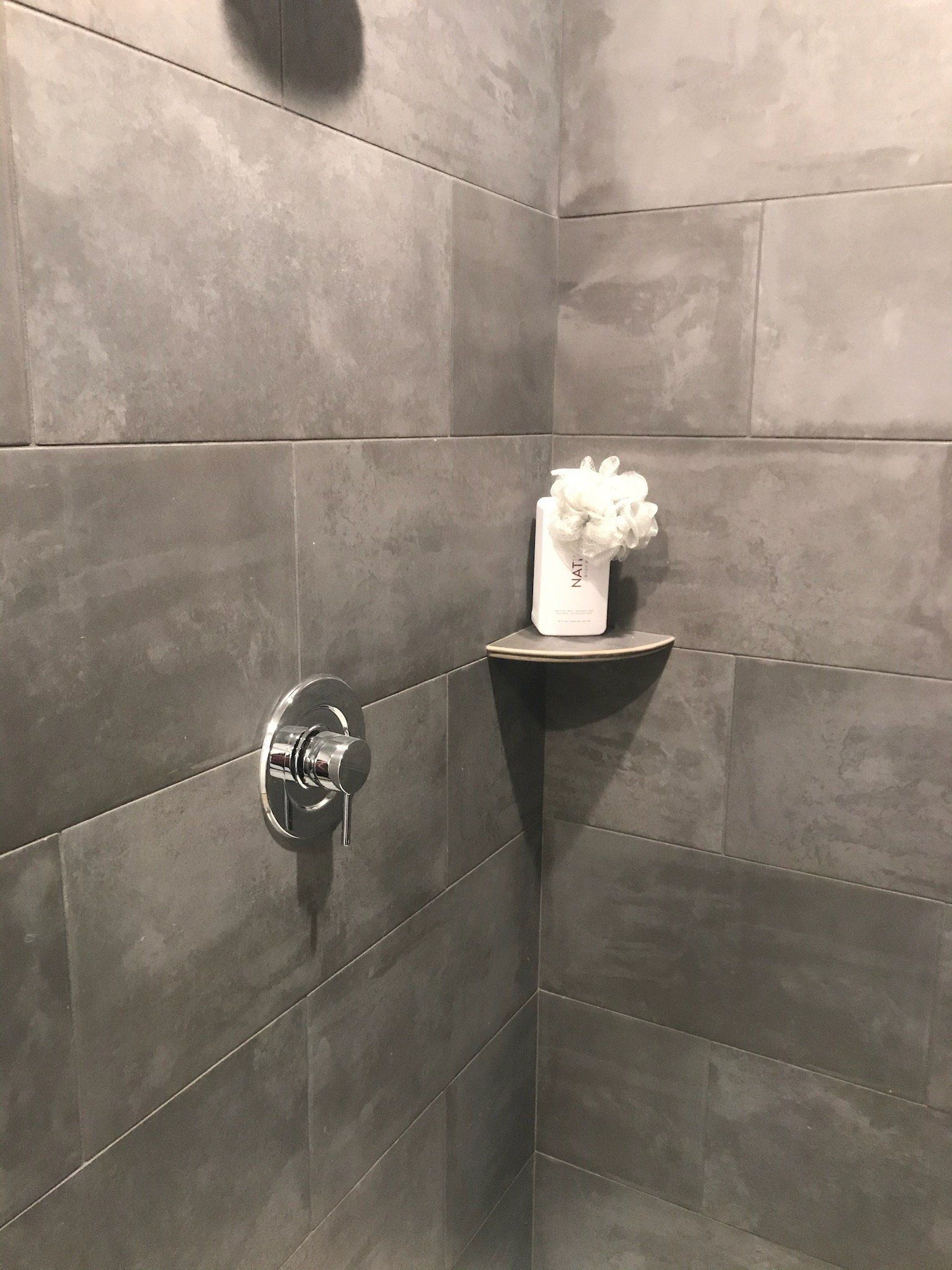 A shower with a shelf and a vase of flowers on it.