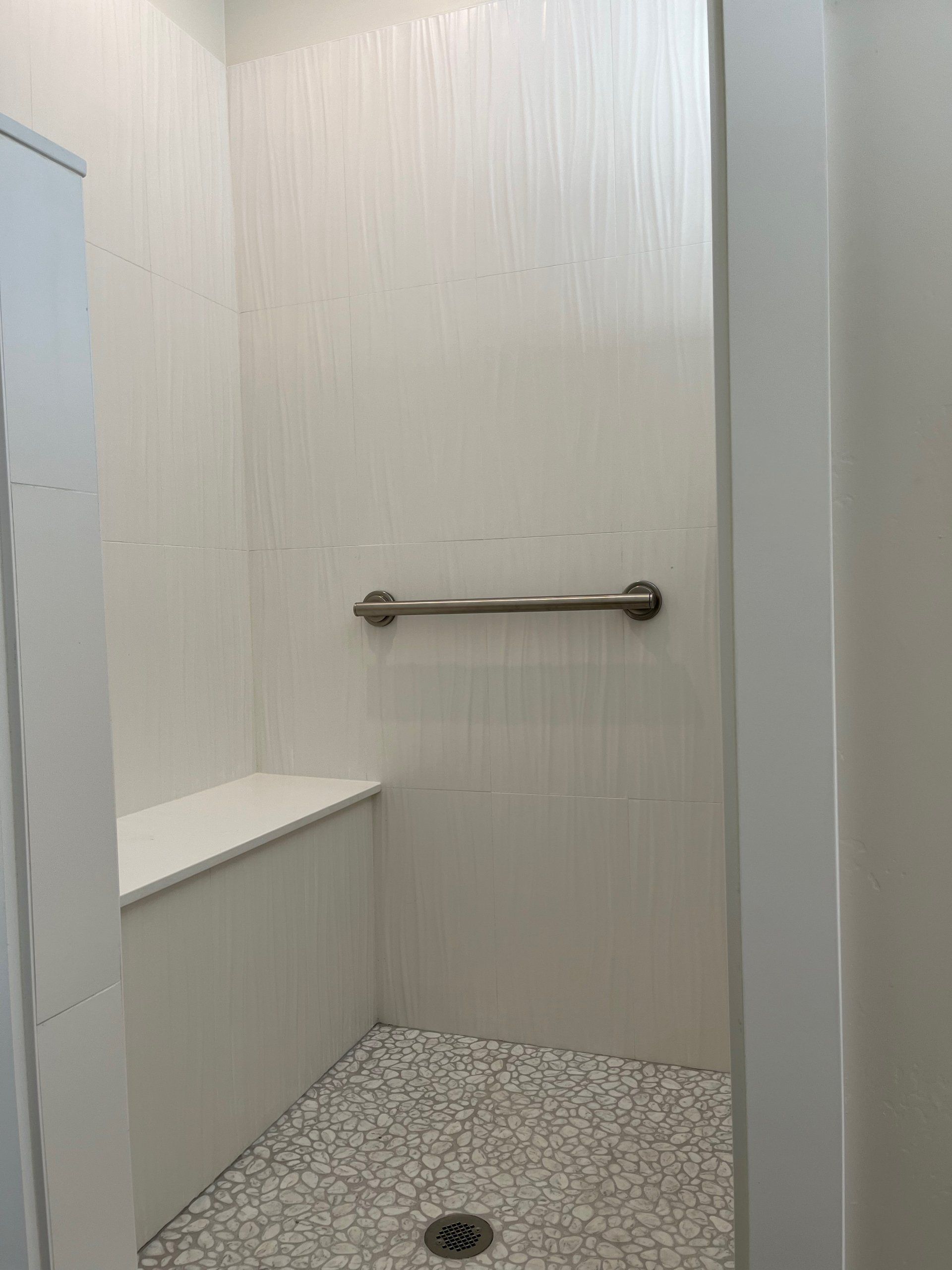 A walk in shower with a bench and a hand rail.