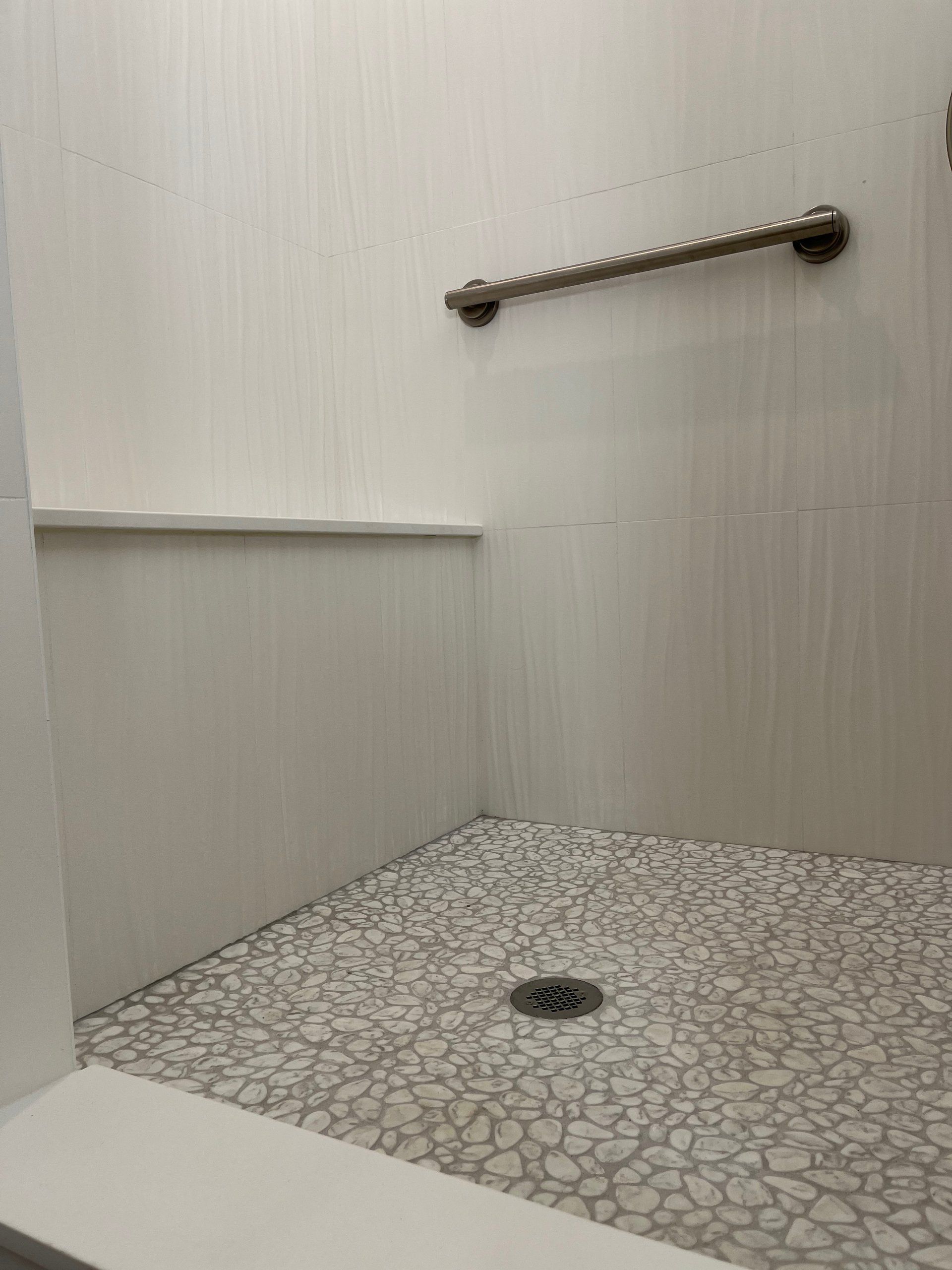 A walk in shower with a hand rail and a drain.