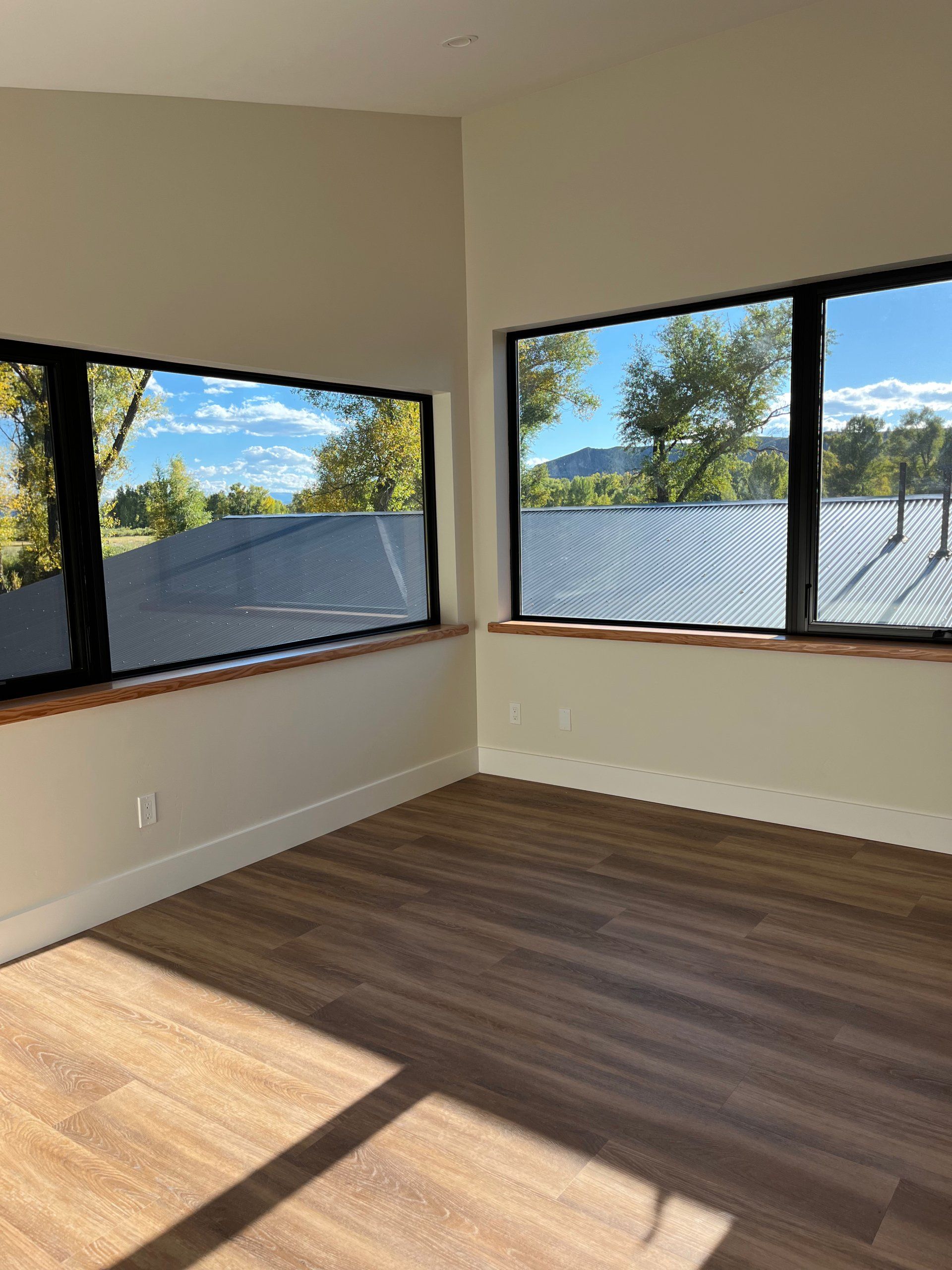 An empty room with two windows and a wooden floor.