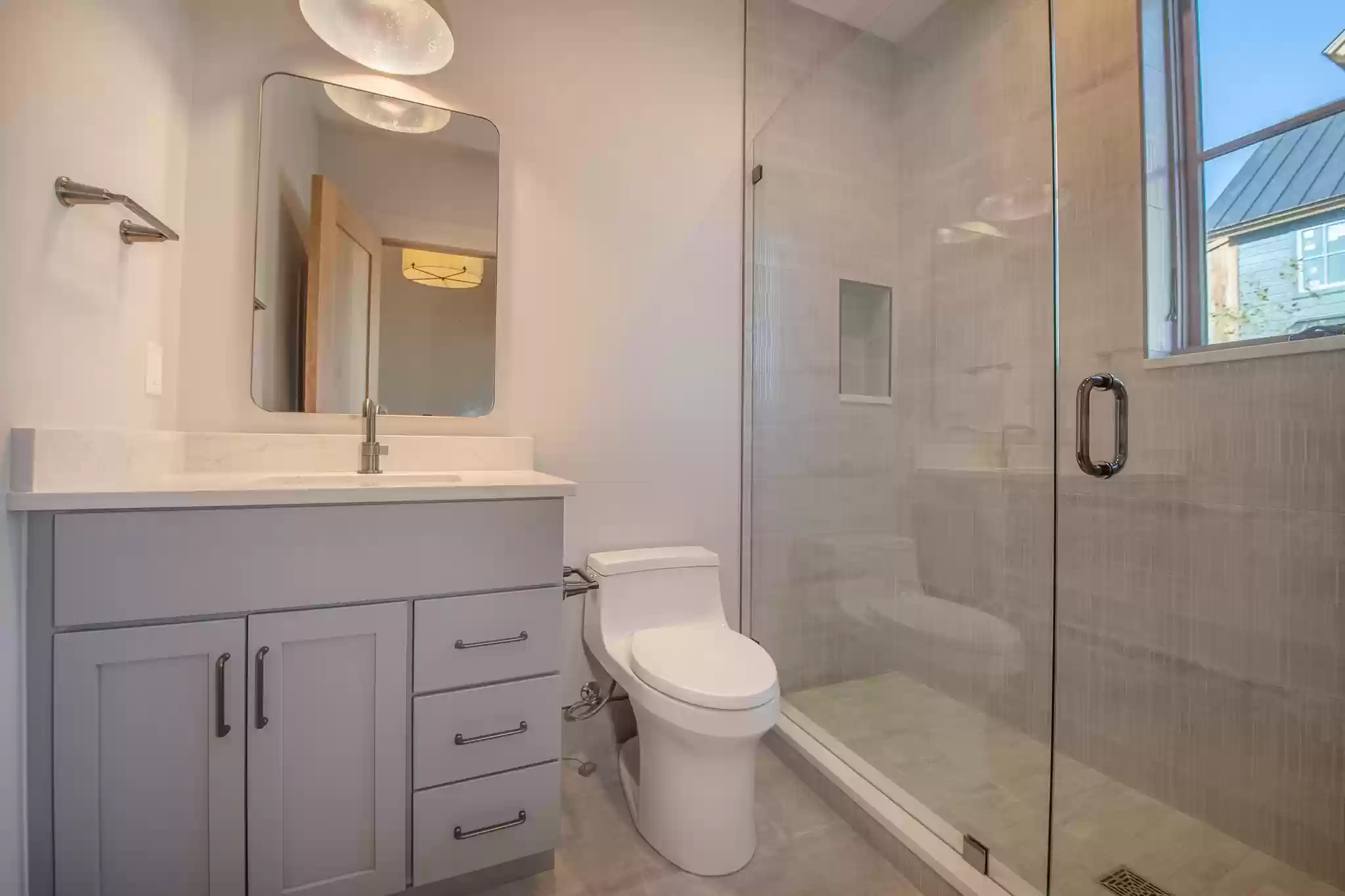 A bathroom with a toilet , sink , mirror and walk in shower.
