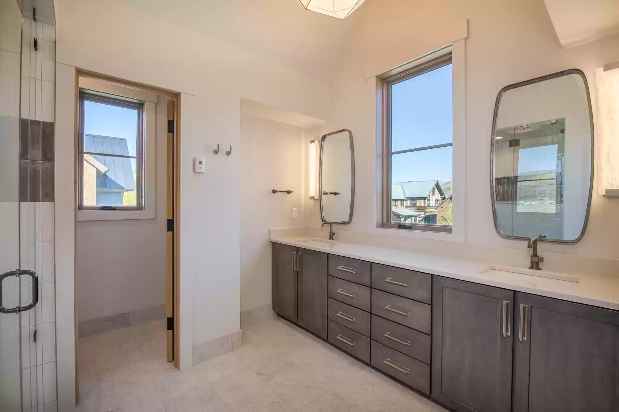 A bathroom with two sinks , two mirrors , and a walk in shower.