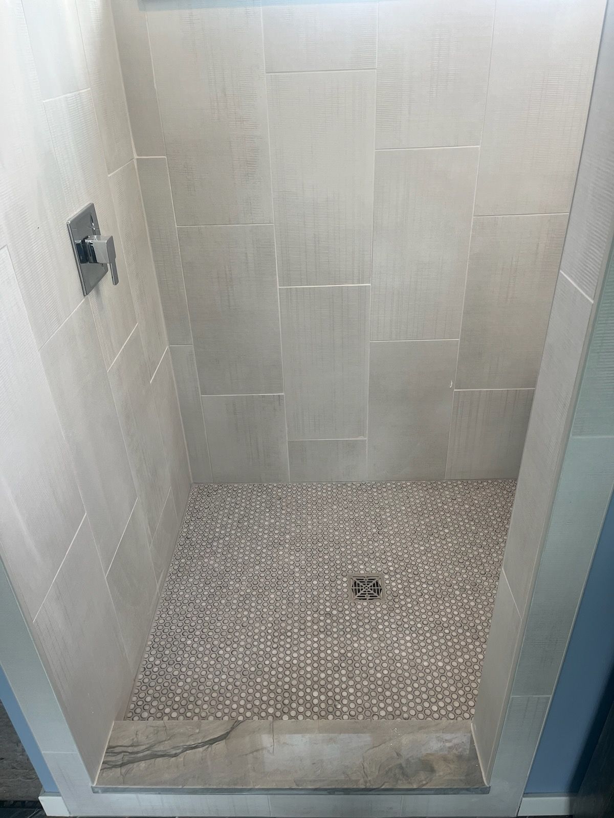 A shower stall with white tiles and a drain in a bathroom.