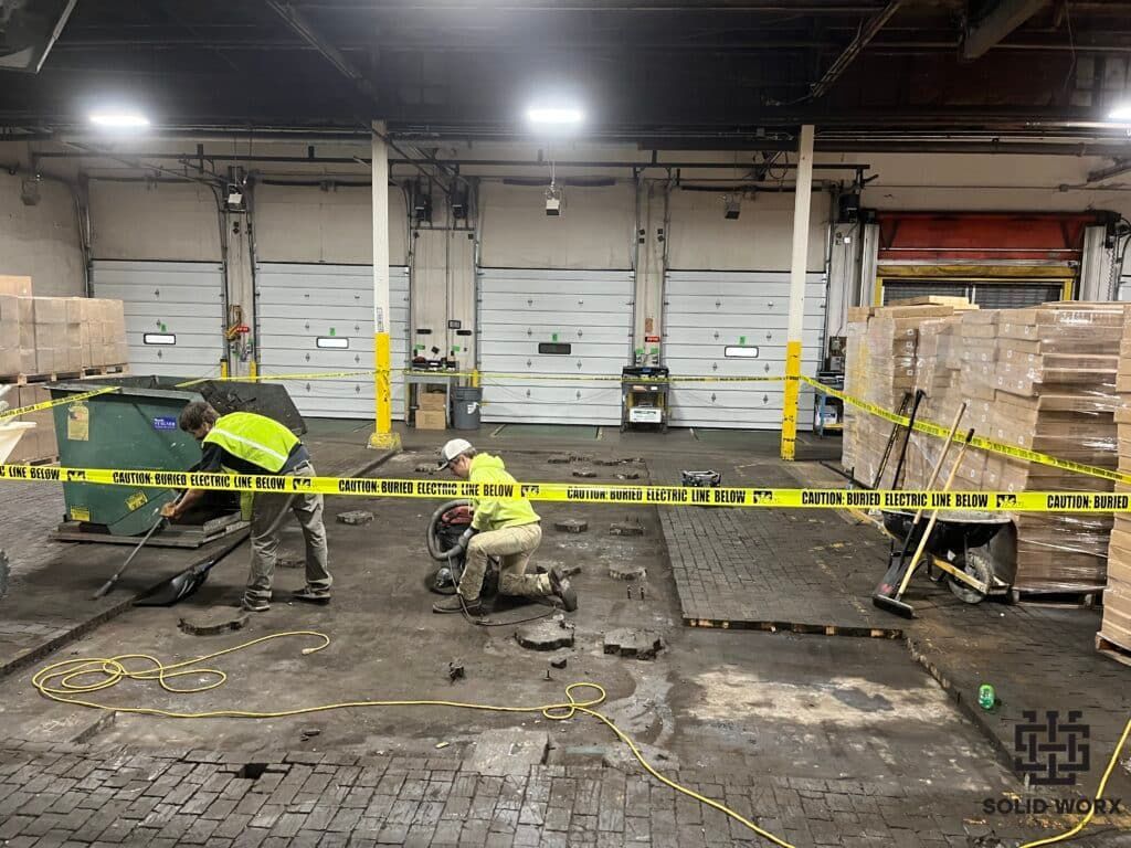 A group of construction workers are working on the floor of a warehouse.