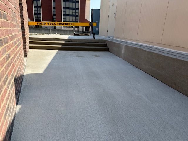 A concrete walkway between two brick buildings with stairs leading up to it.