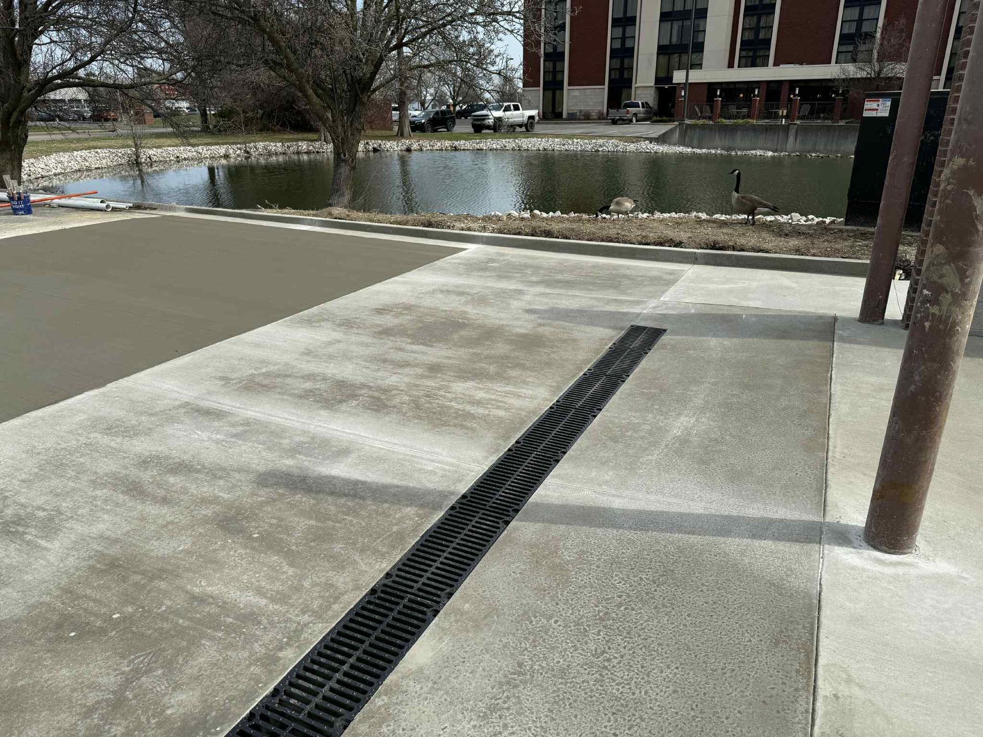 There is a drain on the sidewalk next to a pond.