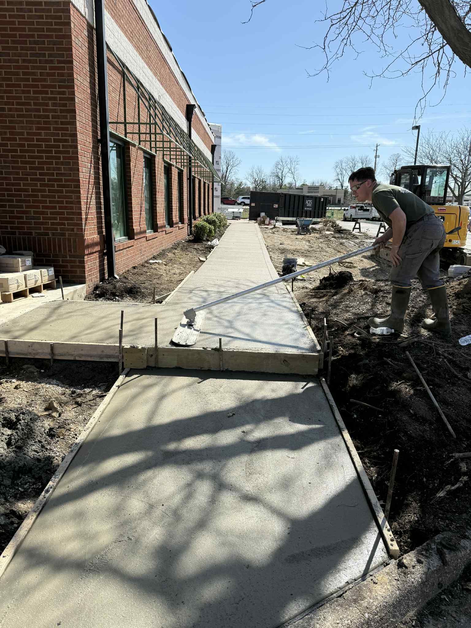 A man is working on a sidewalk in front of a brick building.