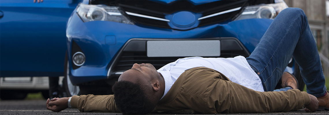 A man is laying on the ground in front of a blue car.