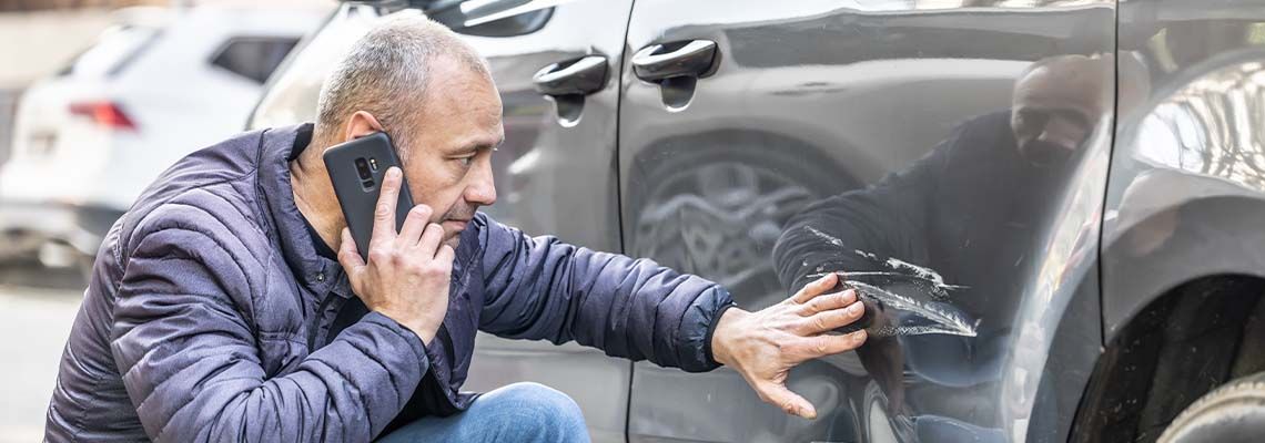 A man is talking on a cell phone next to a damaged car.