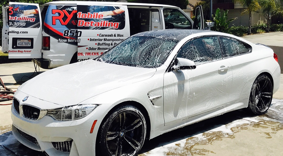 A white bmw m4 is sitting in a parking lot next to a van.