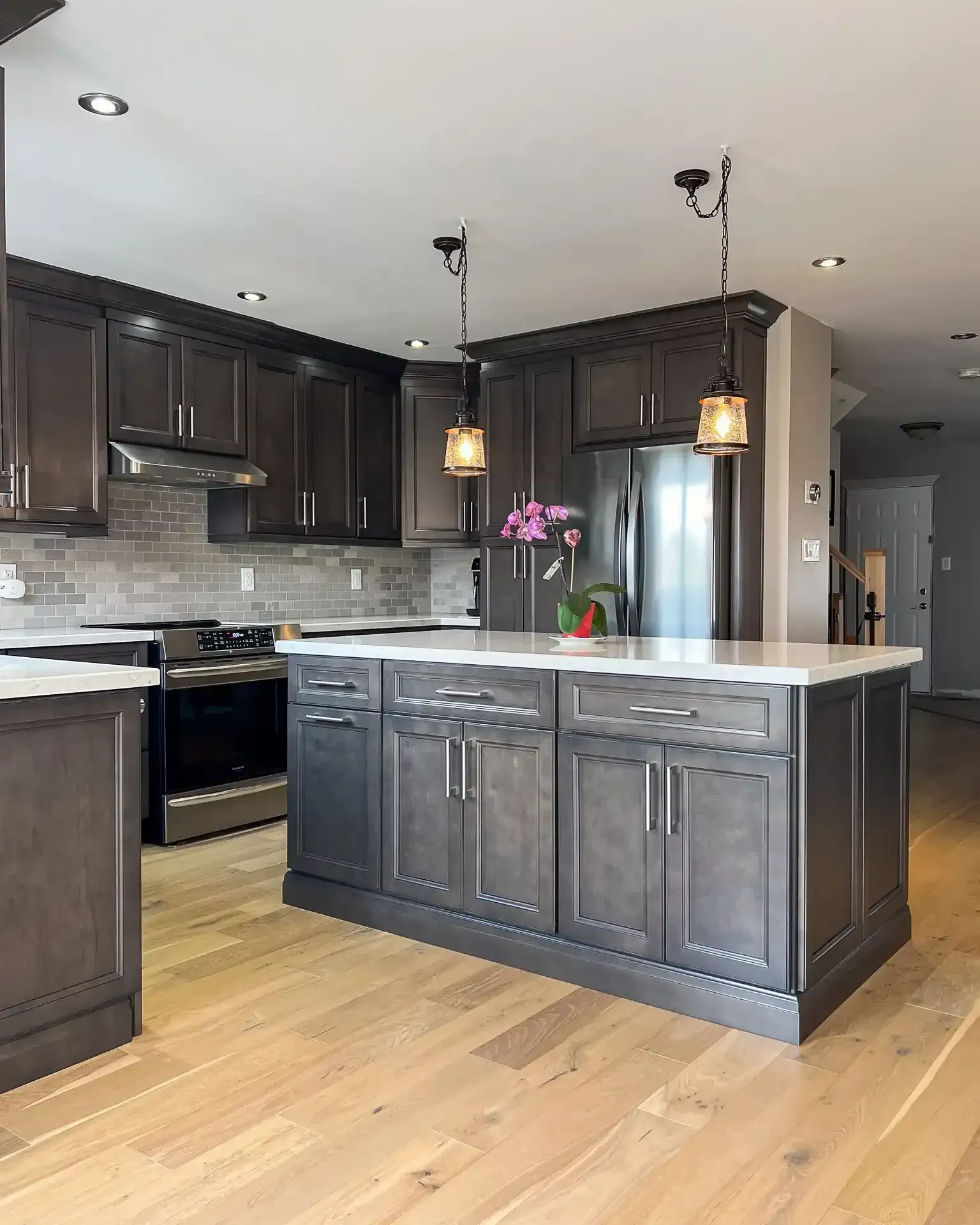 Modern kitchen with dark gray cabinets, light wood floor, and white countertops.