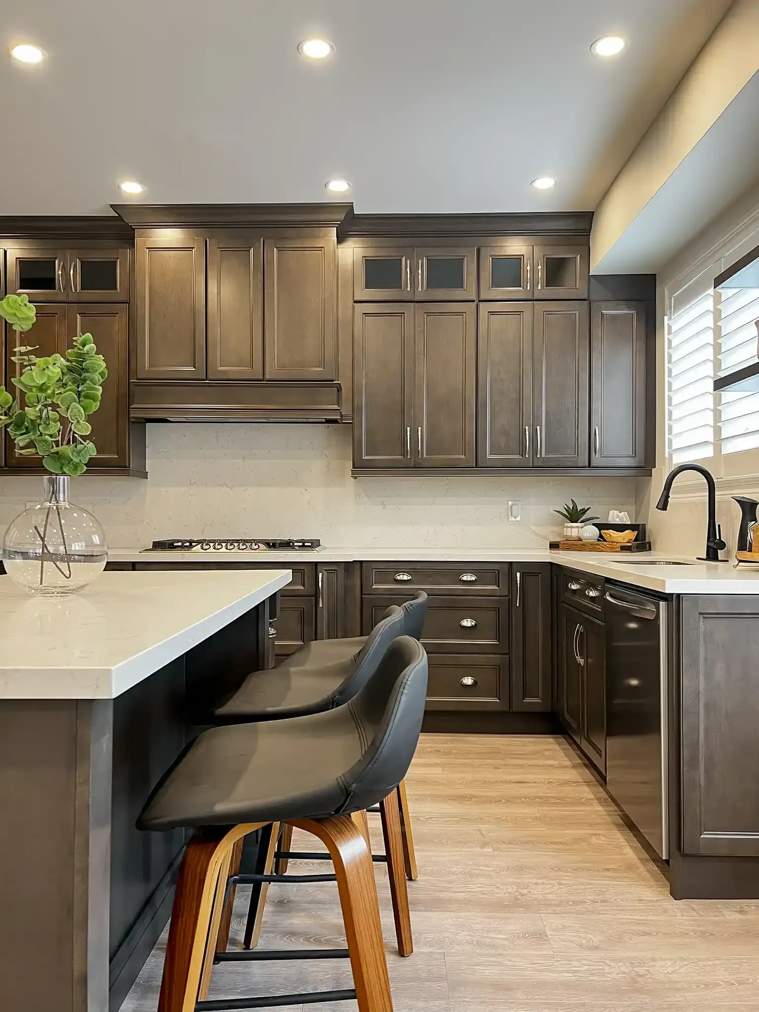 Modern kitchen with gray cabinets, white countertops, and wooden bar stools.
