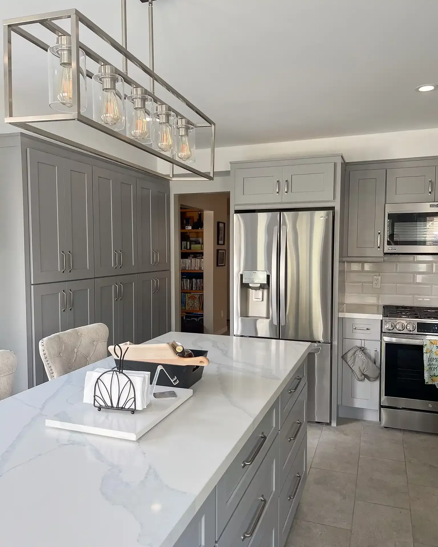 Gray kitchen with large island, stainless steel fridge, and overhead lighting.