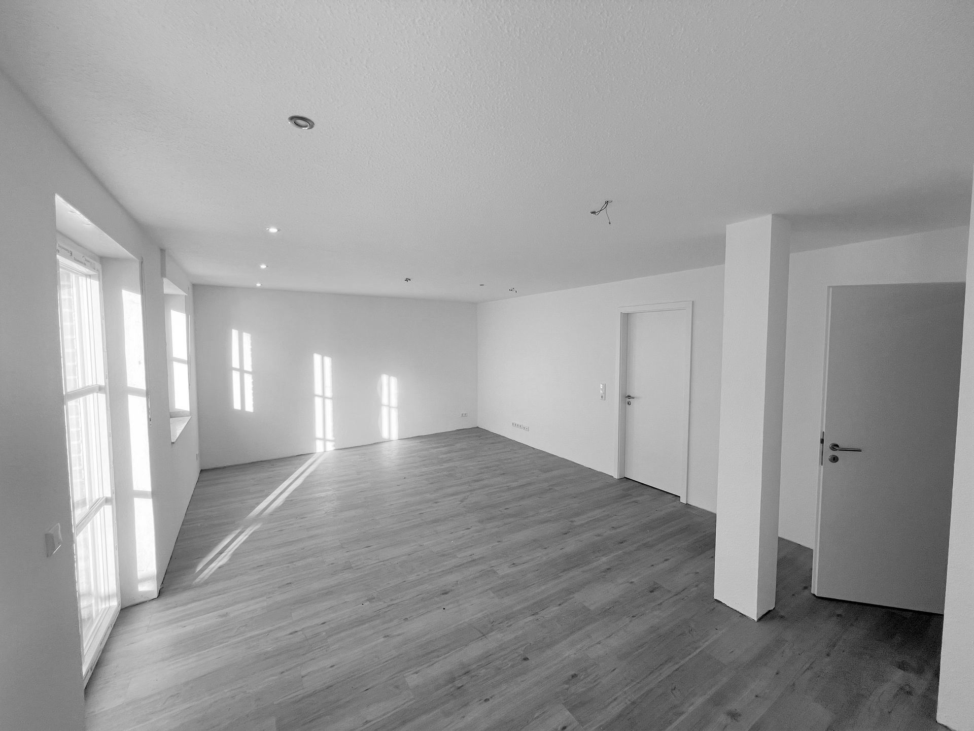 Ein Schwarzweißfoto eines leeren Raums mit Hartholzböden und weißen Wänden.