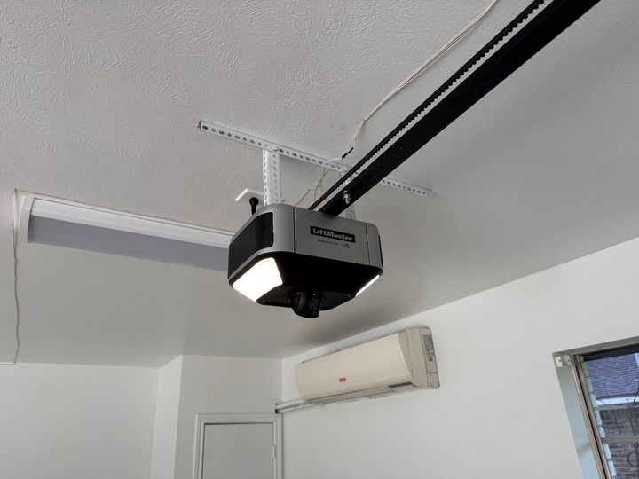 Ceiling-mounted garage door opener on a white ceiling above a wall-mounted AC unit