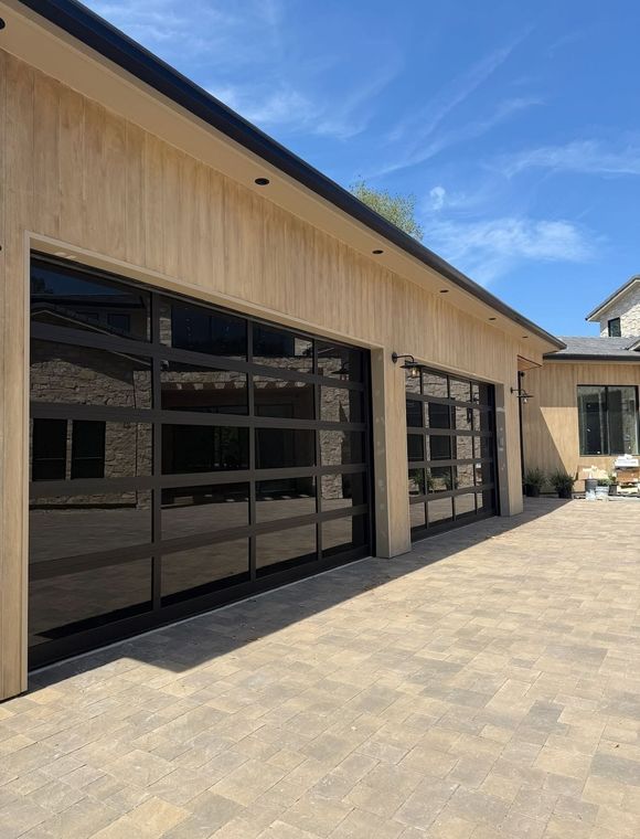 Modern beige building with black garage-style glass doors and a paved courtyard under a blue sky