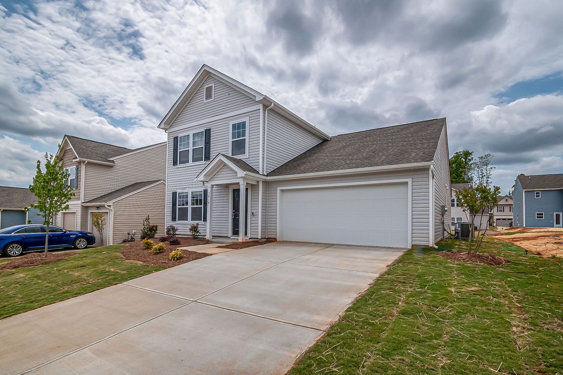 Suburban two-story house with white siding, attached garage, and a concrete driveway under a cloudy sky