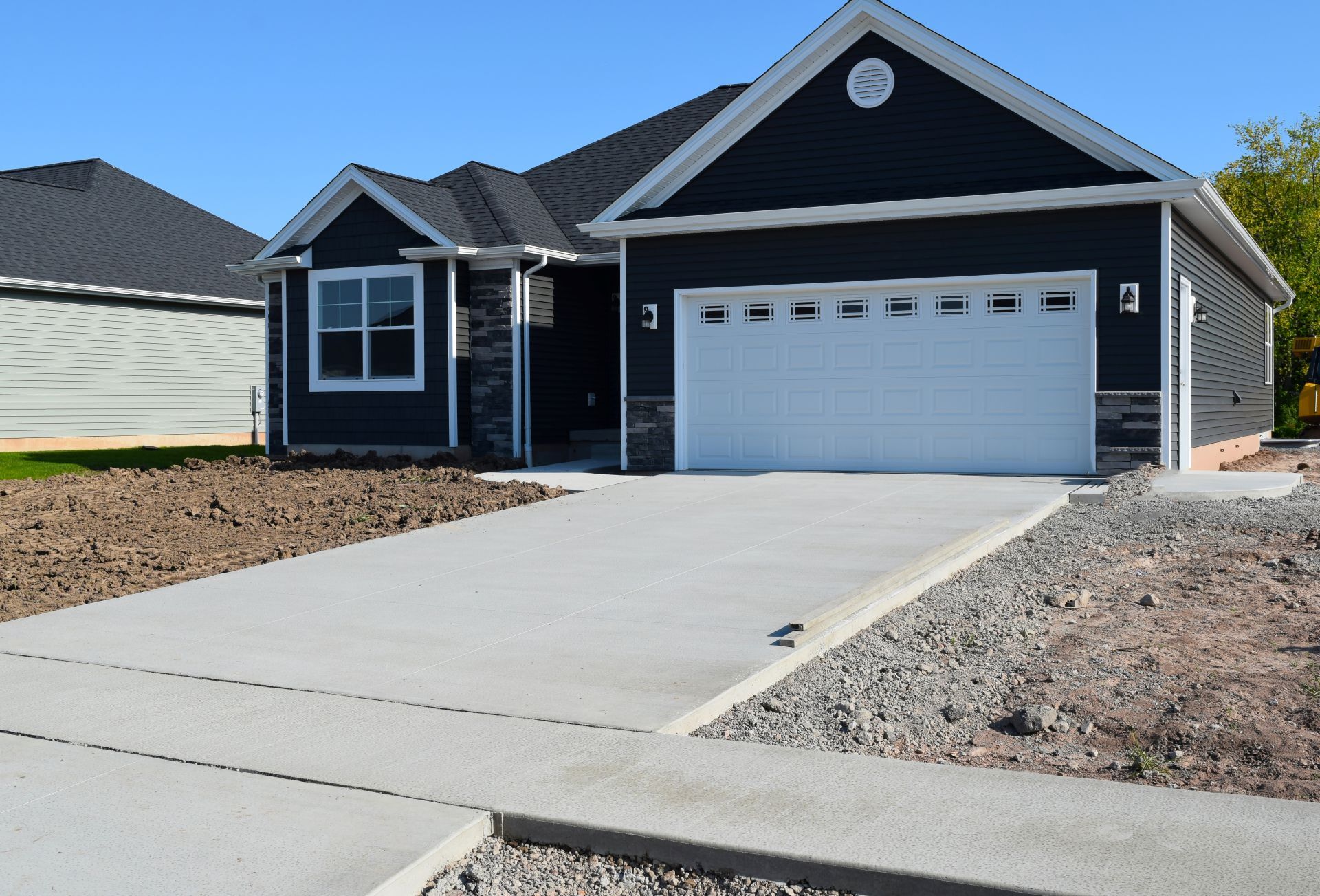 New suburban house with gray siding, white garage door, and a concrete driveway under a blue sky