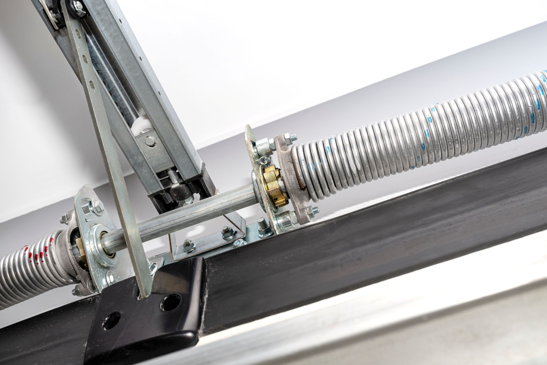 Close-up of a metal garage door torsion spring and shaft with brackets and cables.