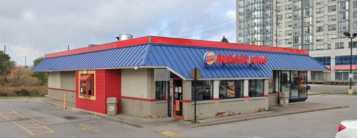 A burger king restaurant with a blue roof is sitting in a parking lot.