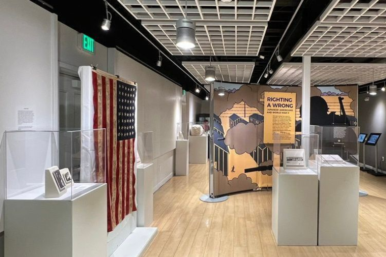 Museum exhibit with American flag on display, and informational panels. Brightly lit with wood flooring.