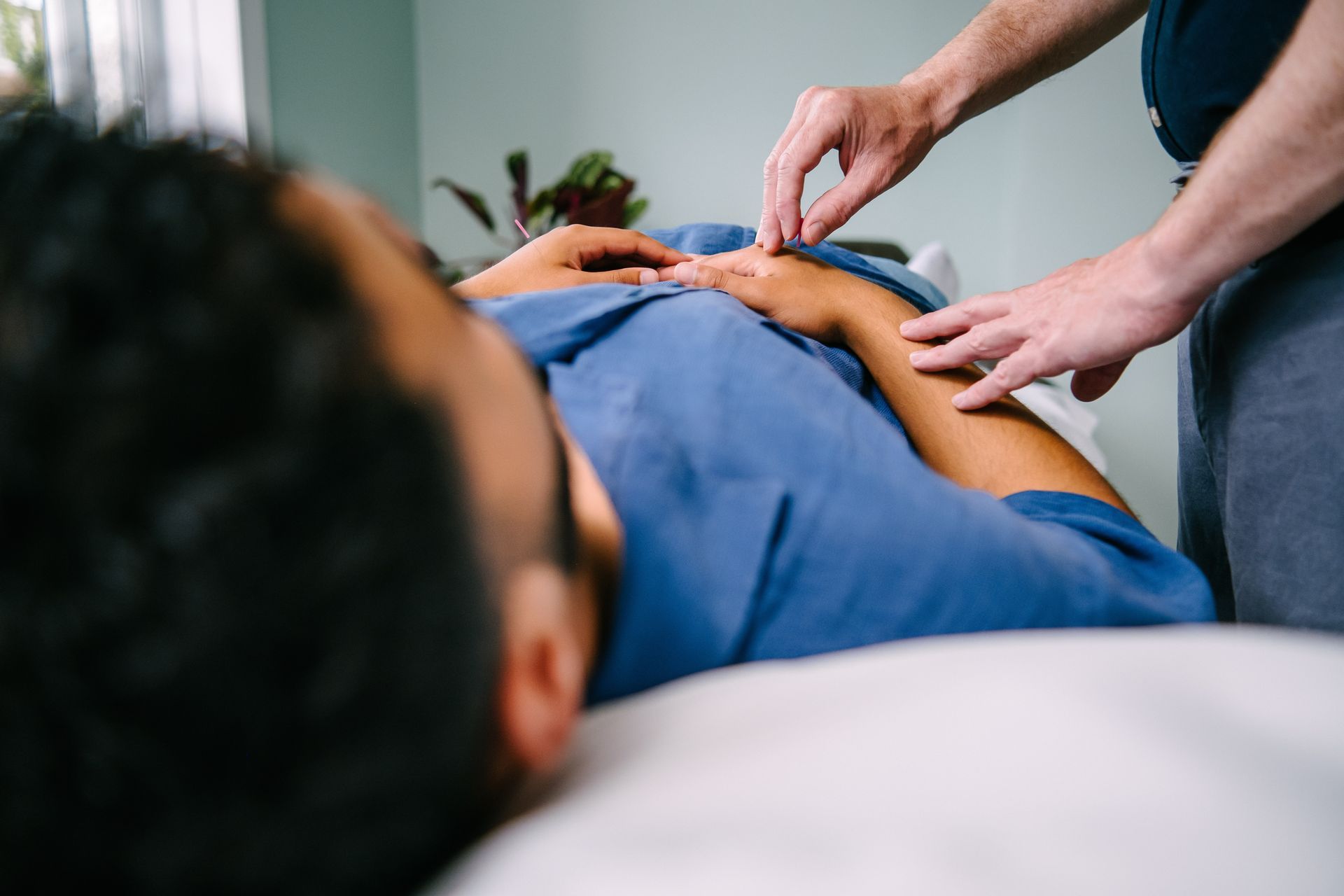 A person receiving acupuncture on their arm, lying on a treatment table. Practitioner is inserting a needle.